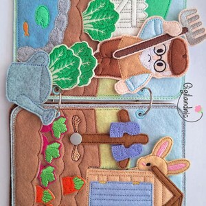 May include: A felt quiet book featuring two pages with farm scenes. The top page shows a gardener with a pitchfork, a pond, and a watering can. The bottom page depicts a carrot patch, a rabbit, and a small house. The text Gigilandnic is visible.