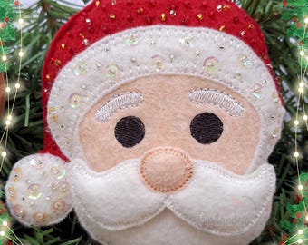 May include: A felt Christmas ornament featuring a Santa Claus face with a white beard and red hat. The ornament is decorated with sequins and beads.