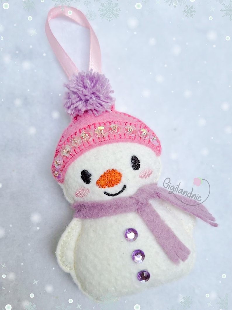 Puede incluir: Adorno navide&ntilde;o de mu&ntilde;eco de nieve hecho a mano con gorro rosa, pomp&oacute;n morado y bufanda. El mu&ntilde;eco de nieve tiene una cara cosida con nariz naranja y ojos negros. El adorno est&aacute; adornado con lentejuelas y tiene una cinta rosa para colgar.