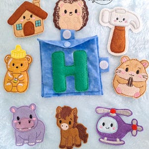 May include: A blue felt square with a green letter H, surrounded by felt shapes including a brown house, a hedgehog, a hammer, a honey bear, a hamster, a purple hippo, a brown horse, and a purple helicopter. The text Gigilandnic is visible.