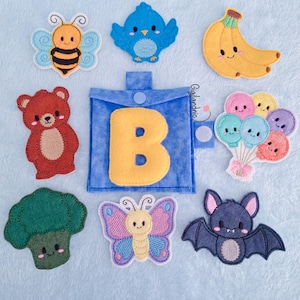 May include: A collection of colorful felt appliques, including a bee, bird, banana, bear, balloons, broccoli, butterfly, bat, and a blue pouch with a yellow letter "B". The appliques are arranged on a light blue surface.