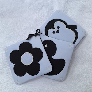 Può includere: Tre bavaglini quadrati azzurri per bambini con disegni ricamati in bianco e nero: un fiore, un pinguino e un'anatra. Ogni bavaglino ha un bordo bianco e un piccolo nastro per appenderlo. I bavaglini sono su una superficie bianca strutturata.