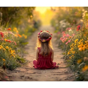 May include: A young girl wearing a red dress and a flower crown sits on a path in a field of wildflowers. The path is lined with colourful flowers, and the sun is shining brightly.