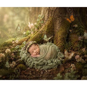 May include: A sleeping infant wrapped in a sage green textured fabric swaddle, wearing a delicate floral headband, resting in a mossy green nest at the base of a large tree surrounded by small pink flowers and several butterflies.
