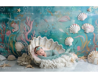 May include: A newborn baby girl is sleeping in a large white seashell prop. The seashell is surrounded by white fluffy fabric and a blue and green mermaid tail. The background is a blue and green ocean-themed backdrop with seashells and coral.