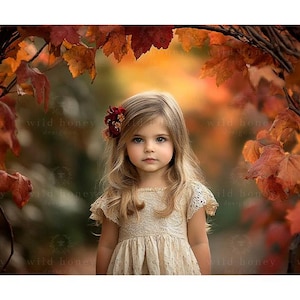 May include: A young girl with long blonde hair wears a cream-colored dress with a floral hair clip. She stands in front of a backdrop of autumn leaves.