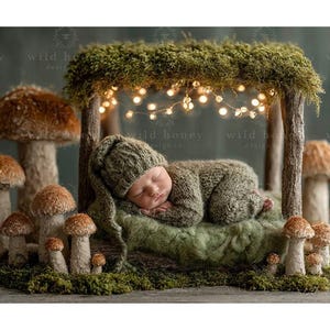 May include: A newborn baby in a knitted green outfit and hat, sleeping peacefully on a green surface. The baby is nestled under a moss-covered canopy with string lights, surrounded by artificial mushrooms of varying sizes. The scene evokes a woodland theme.