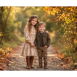 Può includere: Un bambino con un vestito a maniche lunghe a fiori e stivali marroni e un bambino con un maglione verde scuro, una giacca marrone, pantaloni marroni e stivali marroni in piedi su un sentiero circondato da fogliame autunnale e alberi.