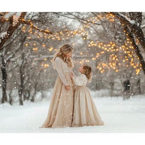 May include: Two people wearing long, white, lace dresses stand in a snowy forest. The trees are decorated with twinkling lights. The person in the front is a child, and the person in the back is an adult.