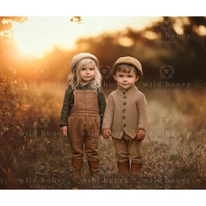 May include: Two children wearing brown and beige clothing stand in a field of tall grass. The girl is wearing a brown overall dress and a brown hat. The boy is wearing a beige sweater and a brown hat. The background is a blurry image of a field with a sunset in the distance.
