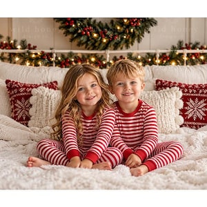 May include: Two children sitting on a bed wearing matching long-sleeved pajamas with horizontal red and white stripes. The pajamas feature a crew neckline and fitted cuffs at the wrists and ankles. The bed is covered with a white textured blanket.