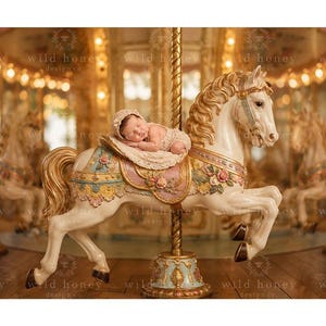 May include: A cream-colored carousel horse with gold accents, floral detailing, and a saddle. A sleeping infant wearing a matching cream-colored bonnet and outfit rests on the saddle. The horse is mounted on a central gold pole.