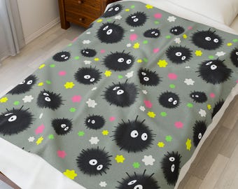 May include: A gray blanket featuring a repeating pattern of black, fuzzy, round creatures with white eyes and mouths. The design includes pink, yellow, and white star and cloud shapes. The blanket is on a bed with a white pillow.