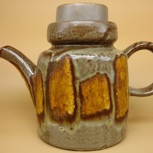 May include: A brown and gray ceramic teapot with a lid and a geometric pattern of brown and yellow glaze.