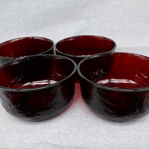 Può includere: Set di quattro ciotole in vetro rosso scuro con superficie testurizzata. Le ciotole sono rotonde e hanno un leggero bordo.