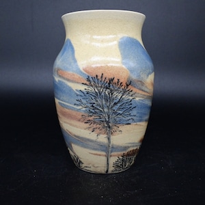 Può includere: Un vaso in ceramica con sfondo marrone chiaro e un design astratto blu e marrone. Il vaso ha una silhouette di albero al centro.
