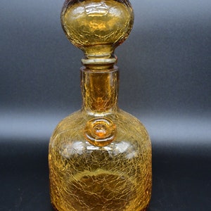Puede incluir: Decantador de vidrio ámbar con un acabado texturizado y craquelado. El decantador tiene un tapón redondo y bulboso.