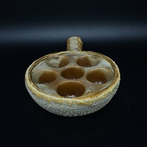 May include: A ceramic dish with six individual wells, perfect for serving escargots or other small appetizers. The dish has a rustic, brown and white glaze and a handle on the side.
