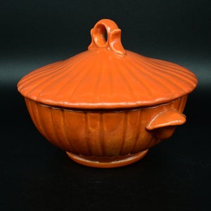 Könnte beinhalten: Eine antike, orangefarbene, überdachte Keramikschale mit geriffeltem Design und einem dekorativen Griff. Die Schale hat eine glänzende Oberfläche und ist perfekt zum Servieren einer Vielzahl von Gerichten.