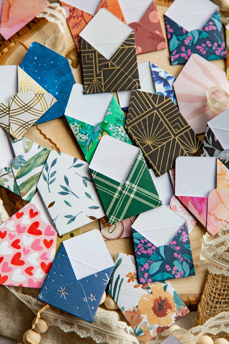 K&ouml;nnte beinhalten: Eine Sammlung kleiner, dekorativer Umschl&auml;ge mit verschiedenen Mustern und Farben, darunter florale, geometrische und abstrakte Designs. Die Umschl&auml;ge sind aus Papier und haben ein wei&szlig;es Innenleben.