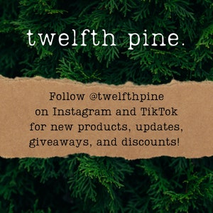 K&ouml;nnte beinhalten: Ein braunes Papierschild mit zerrissenen R&auml;ndern vor einem Hintergrund aus gr&uuml;nen Kiefernnadeln. Auf dem Schild steht "Folge @twelfthpine auf Instagram und TikTok f&uuml;r neue Produkte, Updates, Gewinnspiele und Rabatte!"