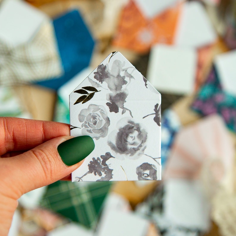 K&ouml;nnte beinhalten: Ein wei&szlig;er Umschlag mit einem floralen Muster in Graut&ouml;nen und Schwarz. Der Umschlag ist in der Mitte gefaltet und hat eine spitze Oberseite.