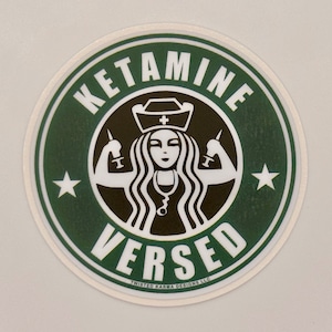 May include: A green and white round sticker with the text "KETAMINE VERSED" in a stylised font. A black and white illustration of a nurse with a syringe in each hand is in the centre of the sticker.