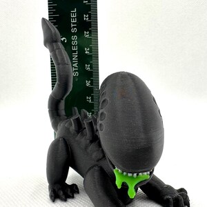 Puede incluir: Una figura de criatura extraterrestre negra impresa en 3D con una sustancia verde que gotea de su boca. La figura mide aproximadamente 12,5 cm de alto y est&aacute; en posici&oacute;n de cuclillas.