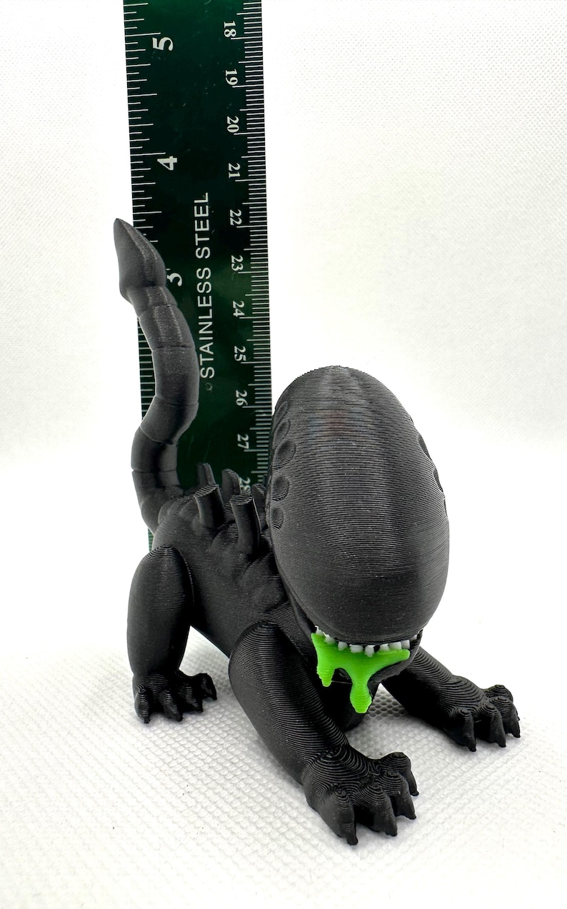 Puede incluir: Una figura de criatura extraterrestre negra impresa en 3D con una sustancia verde que gotea de su boca. La figura mide aproximadamente 12,5 cm de alto y est&aacute; en posici&oacute;n de cuclillas.
