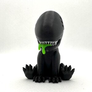 Puede incluir: Una figura de extraterrestre negra impresa en 3D con baba verde goteando de su boca. El extraterrestre tiene una cabeza grande con una boca ancha y dientes afilados. Est&aacute; sentado en cuclillas con los brazos extendidos.
