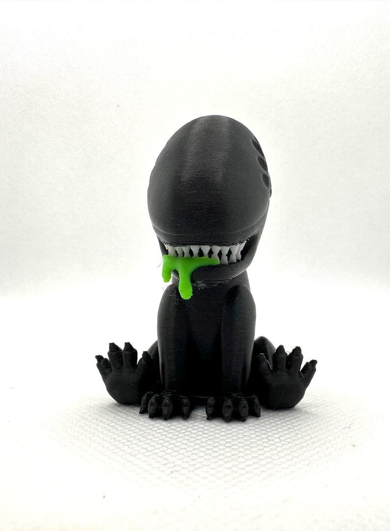 Puede incluir: Una figura de extraterrestre negra impresa en 3D con baba verde goteando de su boca. El extraterrestre tiene una cabeza grande con una boca ancha y dientes afilados. Est&aacute; sentado en cuclillas con los brazos extendidos.