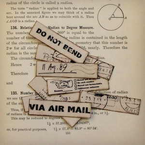 K&ouml;nnte beinhalten: Eine Ansammlung von Vintage-Postetiketten mit Aufschriften wie "DO NOT BEND" und "VIA AIR MAIL". Die Etiketten mit handschriftlichen Daten und Poststempeln sind auf einer Seite eines alten Buches angeordnet.