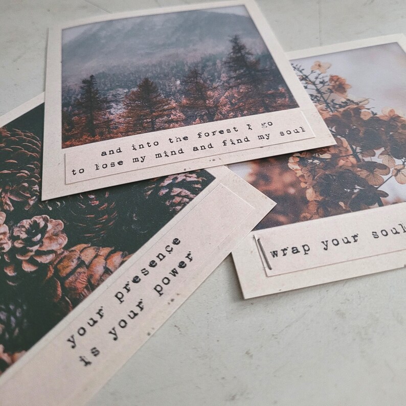 May include: Three brown paper cards with inspirational quotes printed in black text. The first card features a photo of a forest with the text "and into the forest I go to lose my mind and find my soul". The second card features a photo of pine cones with the text "your presence is your power". The third card features a photo of flowers with the text "wrap your soul".