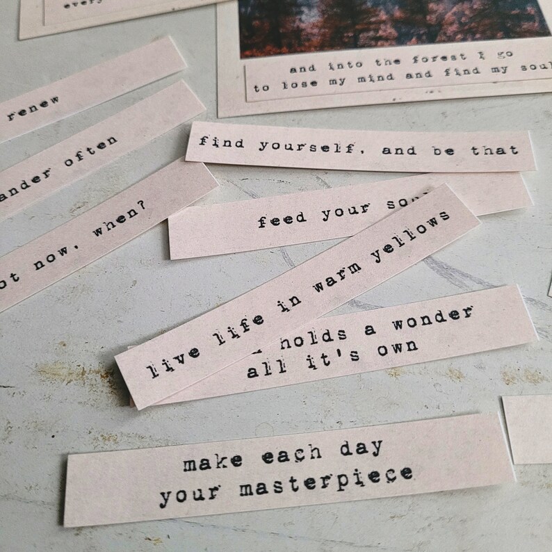 May include: A collection of pink paper strips with inspirational quotes printed in black typewriter font. The quotes include "renew", "wander often", "live life in warm yellows", "make each day your masterpiece", and "find yourself, and be that".