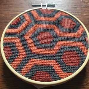 May include: A circular embroidery hoop with a black and orange geometric pattern. The pattern is reminiscent of the carpet from the movie "The Shining".