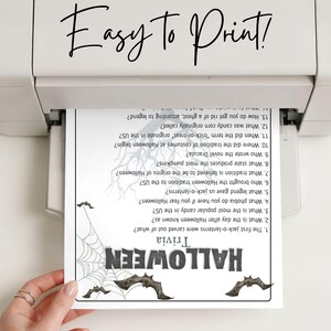 May include: A printed Halloween trivia sheet emerges from a printer. The sheet features a spiderweb and bat graphics, with the word "HALLOWEEN" in bold letters. The text "Easy to Print!" is at the top.