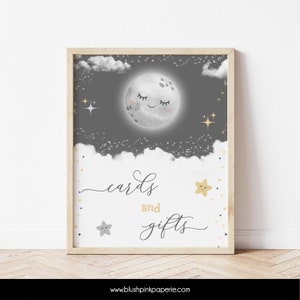 May include: A printable sign with a gray background and a white moon with a smiling face. The moon is surrounded by white clouds and gold stars. The text "cards and gifts" is written in black cursive script.