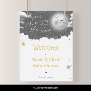 May include: A baby shower welcome sign with a gray background and white clouds. The sign features a cartoon moon with a smiling face and the text "We are over the moon". The text "Welcome to Marie & Chris' Baby Shower" is also included, along with the date "September 24th, 20xx".