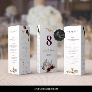Könnte beinhalten: Eine weiße Tischnummerkarte mit einer burgunderfarbenen Nummer 8, goldenem Text, der "Tisch" sagt, und einer Aquarellillustration eines Schlosses mit roten Rosen. Der Text "Luy & Connor" und das Datum "06-02-2023" sind in Schwarz unterhalb des Schlosses gedruckt. Die Karte ist für einen Hochzeitsempfang konzipiert.