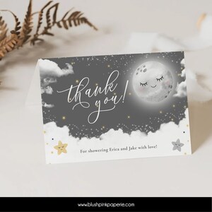 May include: A gray thank you card with a white moon and stars on a dark gray background. The text "thank you!" is written in white cursive. The text "For showering Erica and Jake with love!" is written in black. The website "www.blushpinkpaperie.com" is written in black at the bottom of the card.