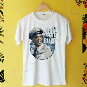 Könnte beinhalten: Weißes T-Shirt mit einem Grafikdruck eines Mannes in Polizeiuniform mit dem Text "Nip it in the bud!"