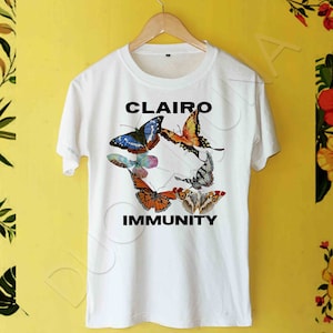May include: White t-shirt with a black graphic of butterflies and the text "CLAIRE" and "IMMUNITY".