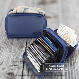 May include: Two navy blue zippered wallets, one closed and one open, displaying cash and credit cards. The closed wallet has the initials "ADR" engraved. The open wallet shows the interior card slots and the text "CUSTOM ENGRAVING".