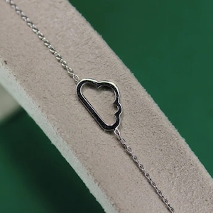 Könnte beinhalten: Ein silbernes Kettenarmband mit einem Wolken-Anhänger. Die Kette ist zart und der Anhänger ist schlicht und elegant.