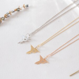 K&ouml;nnte beinhalten: Drei zarte Halsketten mit Kolibri-Anh&auml;ngern. Jeder Anh&auml;nger hat ein ausgeschnittenes Herzdesign. Die Halsketten sind in Silber, Gold und Ros&eacute;gold dargestellt.