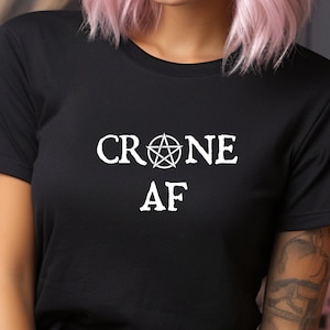 May include: Black t-shirt with white text that reads "CRONE AF" with a pentagram symbol between the words.