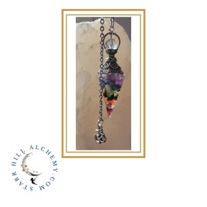 May include: A silver and crystal pendulum with a clear crystal point and a silver chain. The pendulum is filled with colourful crystals in a rainbow pattern.