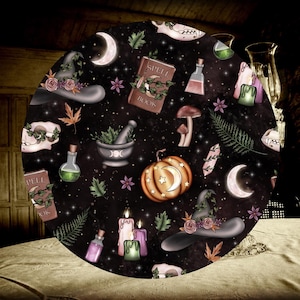 May include: A black and white round tablecloth with a witchy theme. It features a variety of illustrations including a witch's hat, a cauldron, a spell book, a pumpkin, and a crescent moon. The tablecloth has a dark background with a starry pattern.
