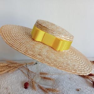 May include: A wide-brimmed straw hat with a bright yellow ribbon around the crown. The hat is a natural, light brown colour and has a circular design. This hat is a stylish accessory, perfect for sun protection or fashion.