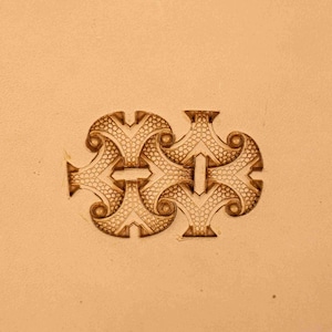 Puede incluir: Primer plano de una superficie de cuero marrón con un diseño en relieve simétrico y detallado. El diseño presenta formas entrelazadas con un patrón punteado texturizado y bordes curvos, creando un elemento decorativo.
